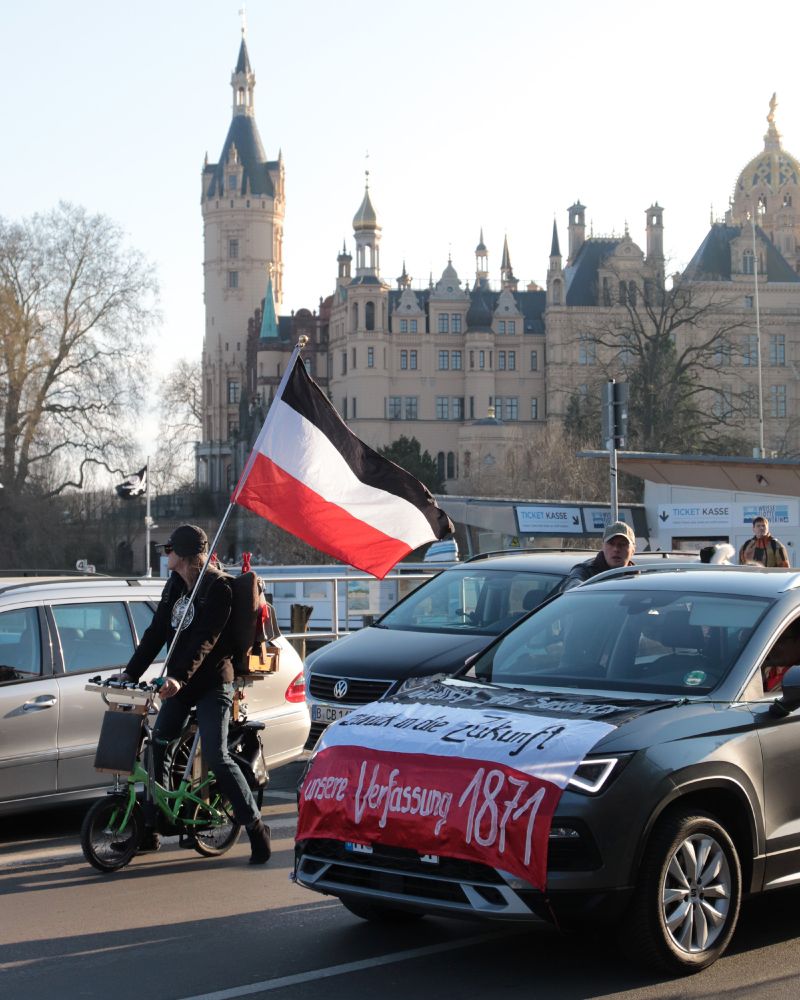 Zu sehen sind ein Fahrradfahrer mit einer Reichsflagge sowie ein Auto, auf dem ebenfalls eine Reichsflagge befestigt ist. Es folgen weitere Fotos von der Demonstration.