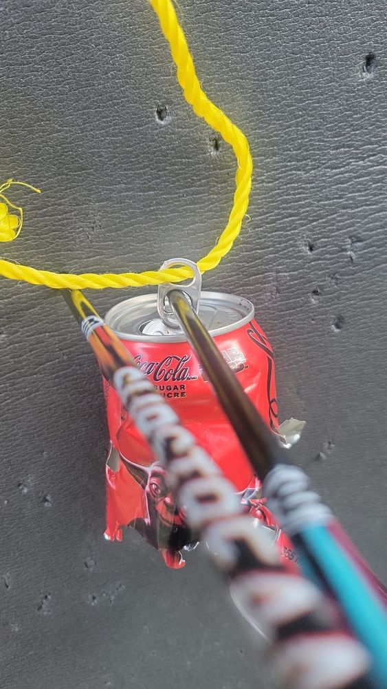 An arrow has gone through one of the holes in the tab on top of a coke can being used for target practice. 