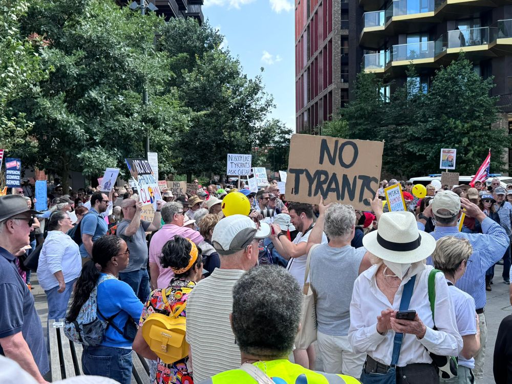 Crowd of people, some carrying signs. One sign prominently in view says, 