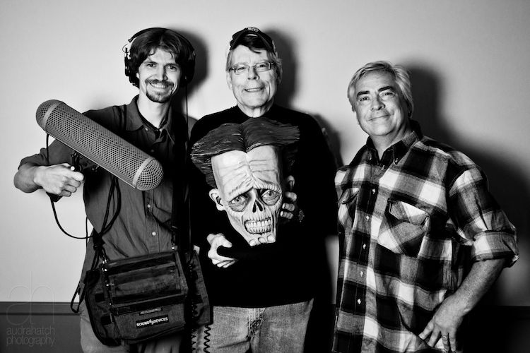 Photo of Fred Greenhalgh, left, with audio equipment, Stephen King American novelist in center, holding mascot from his radio station WKIT in Bangor, Maine, and audio drama director Bill Dufris, far left.