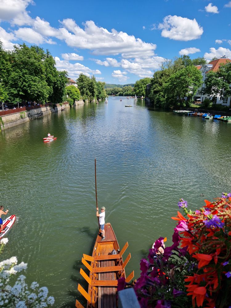 A man is standing on a Stocherkahn in the Neckar river in Tübingen on a sunny day
