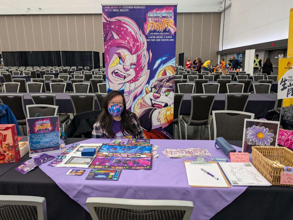 Amanda Panda at the Violet Diasy Table in Proto Alley of Terminal City Tabletop Con in front of the Popcats Fighter prototype and banner. 