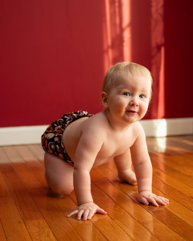 A baby modeling a mushroom cloth diaper print while crawling and smiling at the camera