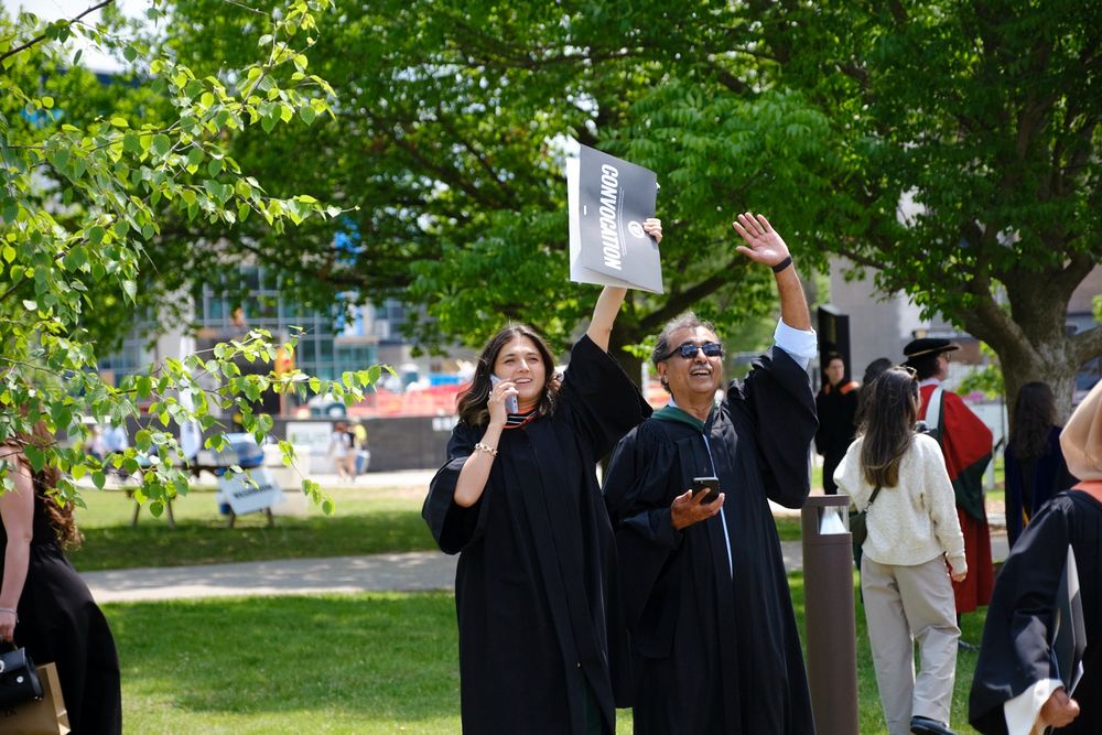 A new environment grad and a parent waving at others while celebrating outside