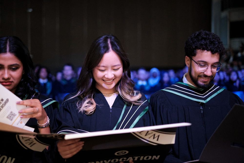 An arts grad who recently crossed the stage at the PAC looks on and smiles at her diploma