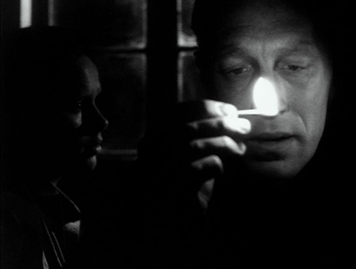Frame from Hour of the Wolf in which Max Von Sydow holds a match in front of his face while Liv Ullmann sits in darkness behind him. 