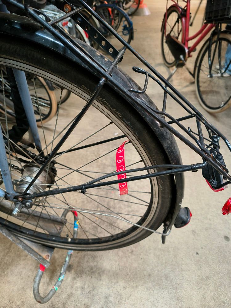 rear wheel of a bicycle in a parking rack, with a red tag round one of the spokes