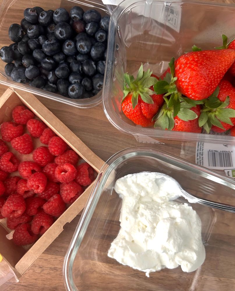 A glass bowl filled with creamy Greek yoghurt, surrounded by fresh punnets of strawberries, raspberries and blueberries. A colourful, healthy brunch! 