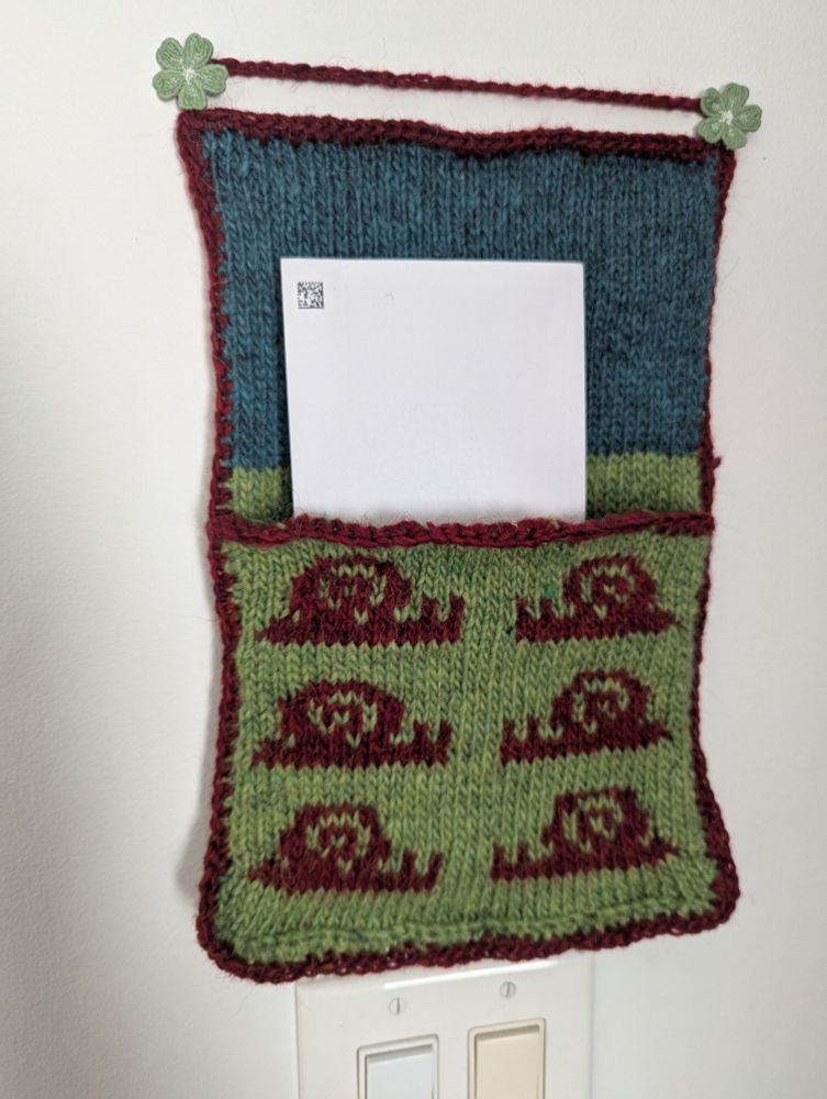 Knitted bag for holding mail. There's a snail pattern.