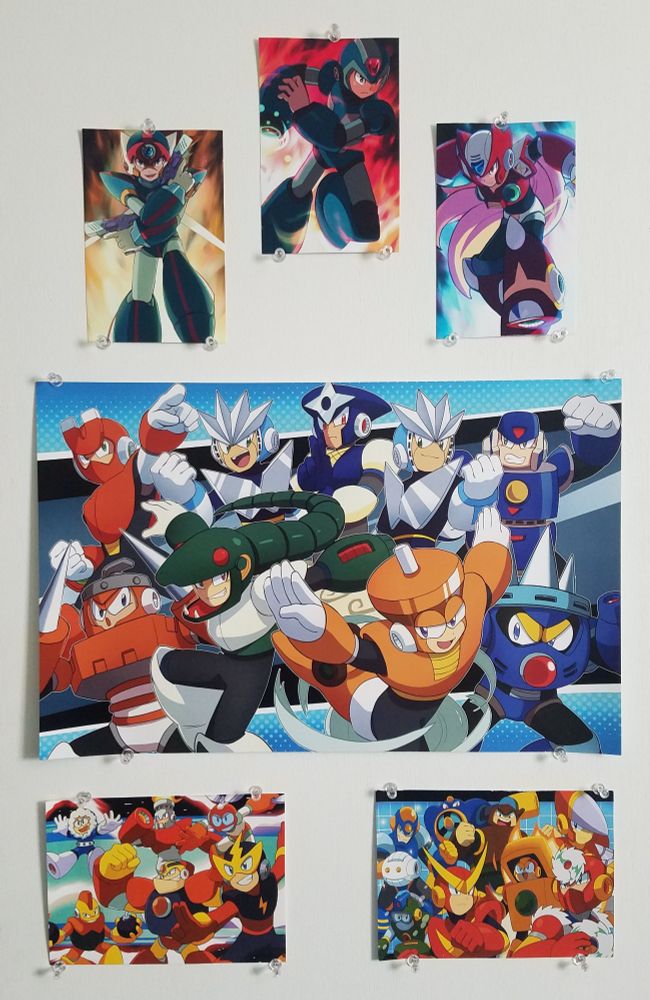 A photo of six Mega Man posters held up by pins.
The top three feature Axl, X, and Zero respectively; the center one features the Robot Masters from MM3; the bottom left features the Robot Masters from MM1; and the bottom right features the Robot Masters from MM2.