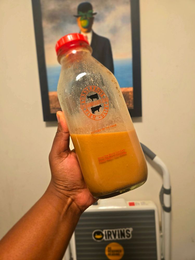 A glass milk bottle filled with coconut milk seasoned into a golden/brownish hue.