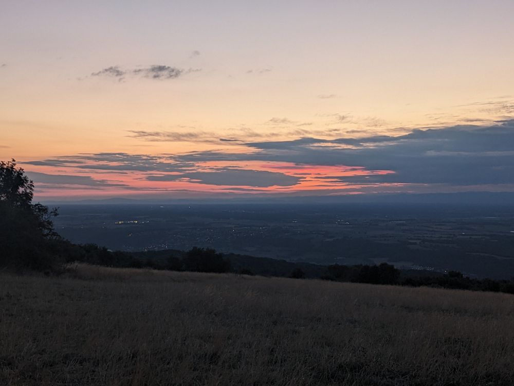 Photo de paysage pris depuis le haut d'un petit mont, ciel très matinal avec les lueurs du soleil derrière les nuages a l'horizon
