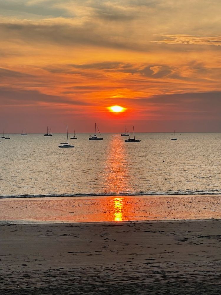 Sun setting over water with boats on the water. Sun reflected off the surface. Light clouds overhead.