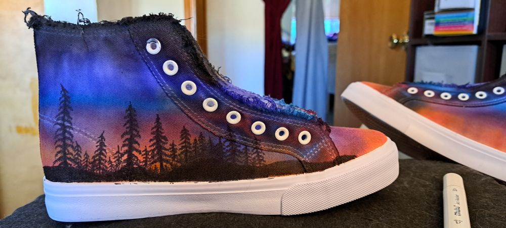 Canvas shoes painted with a vivid scene of trees silhouetted against a sunset. 