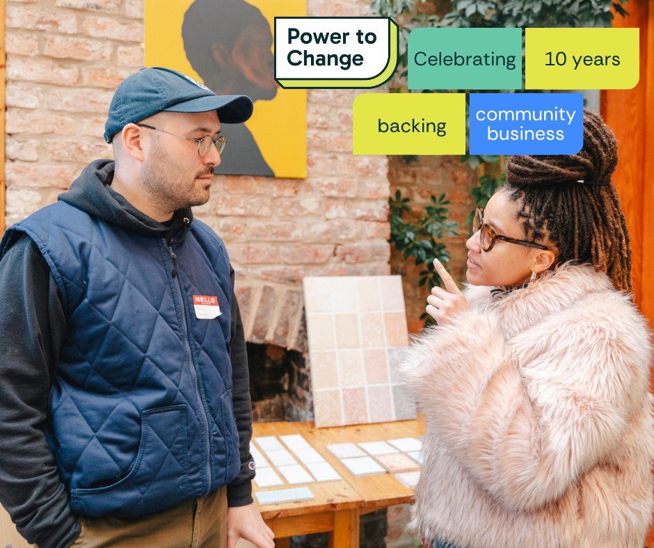 Two individuals engage in conversation at an event celebrating 10 years of community business, sponsored by Power to Change. One person gestures towards a display board while the other listens intently.