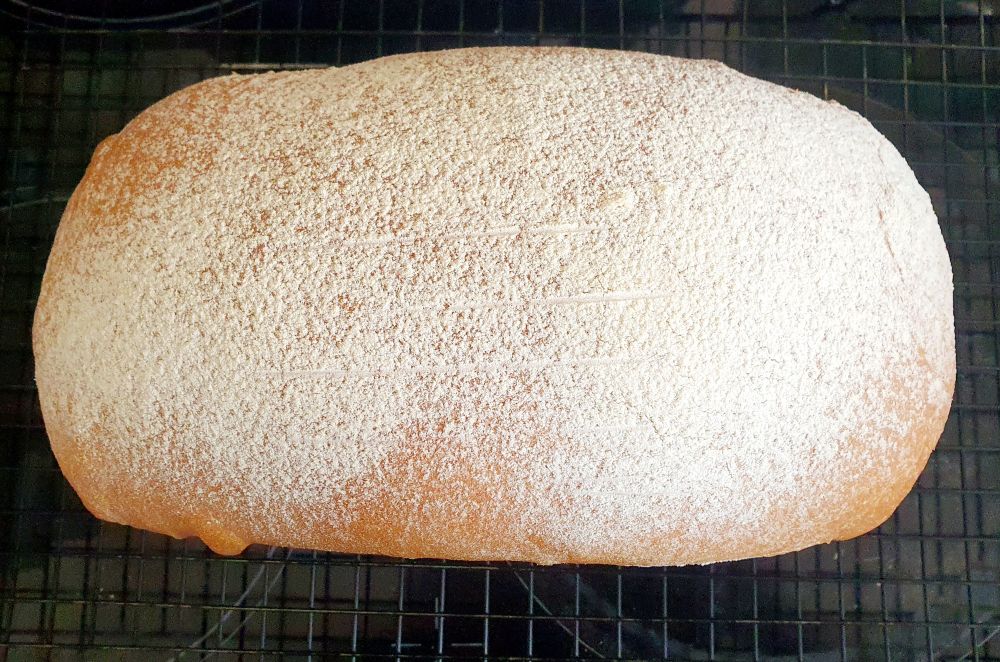 Top down look at a white bread loaf, baked in a 2lb loaf tin. It is topped with sieved bread flour.