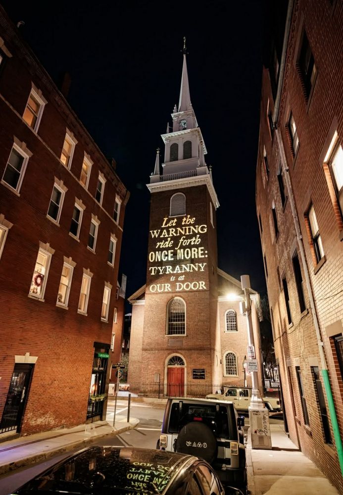 Photo of the Old North Church in Boston illuminated with the words "Let the warning ride forth once more: tyranny is at our door."