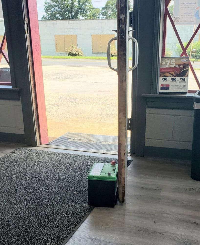 A shop door propped open by a car battery on the floor