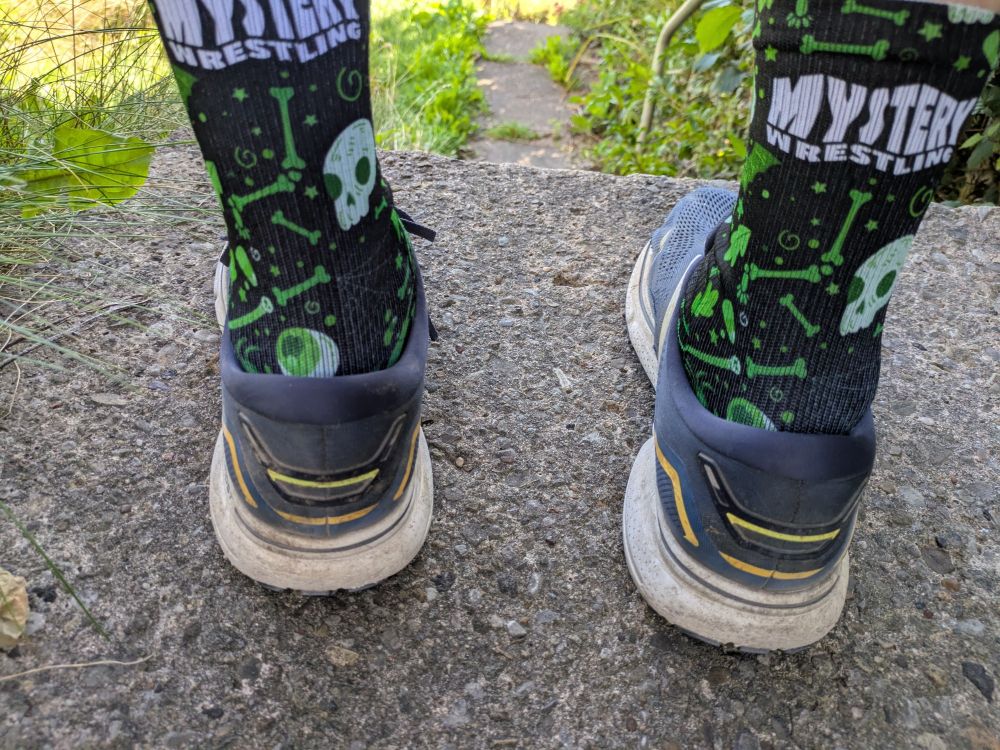 Black socks with glow in the dark skulls, eyes and bones, and white text reading Mystery Wrestling, located at the end of my getaway sticks.