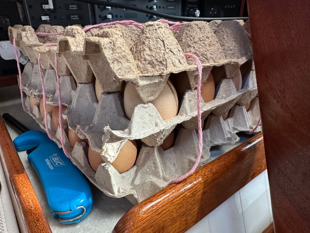 2 flats of 30 eggs each, sandwiched between egg carton cardboard and tied together with pink yarn, sit on a fiddle-edged counter on a small sailboat. Prepping for a pacific voyage. These should last the duration of 4-6 weeks at sea, if we don’t eat them first. 