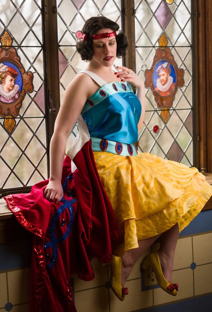 Seated on a windowsill in an art deco version cosplay of Snow White. 