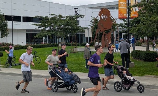 People running and pushing strollers on Wilson Avenue, past the Port Coquitlam Community Centre and its new Terry Fox sculpture.    