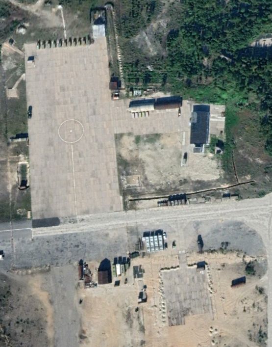Screenshot from Google Earth, August 2022. In the lower right corner rectangular concrete elements are being laid out to create a pad. There seemsto be gabions and  a double fence on three sides of the pad. Directly to the northwest of the pad are four white, rectangular containers, each approximately 10 meters long.