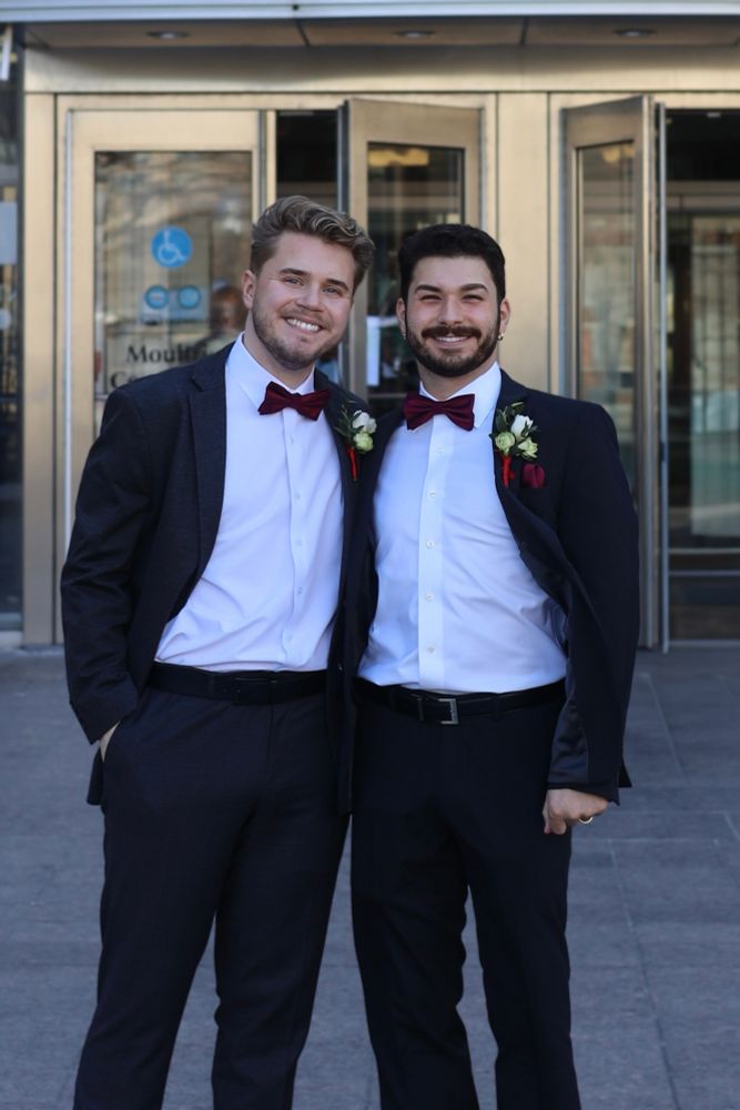 Two husbands wearing suits with burgundy bow ties celebrating their marriage in front of a courthouse!