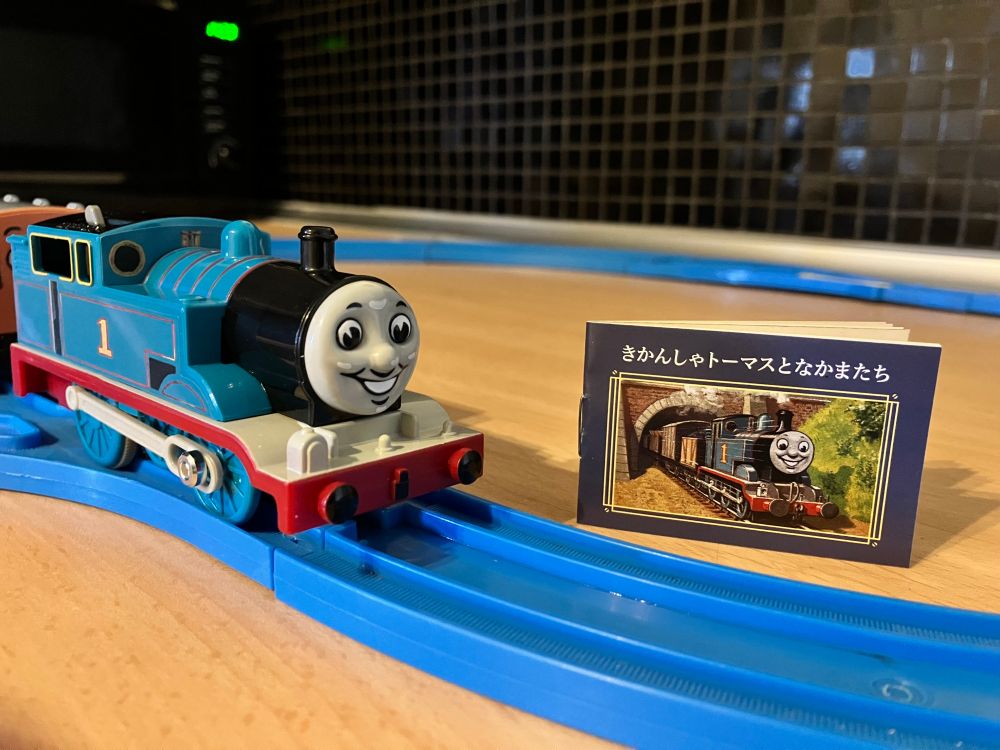 The Plarail 80th anniversary Thomas standing next to the little booklet it comes with