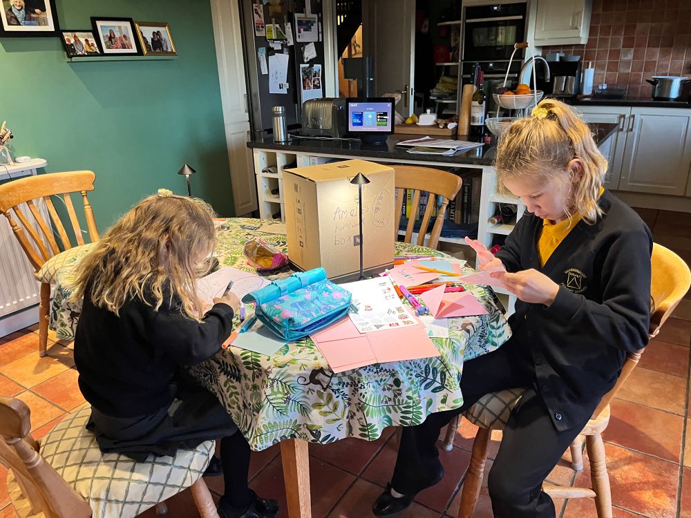 Two children sitting at the table drawing pictures on Christmas cards