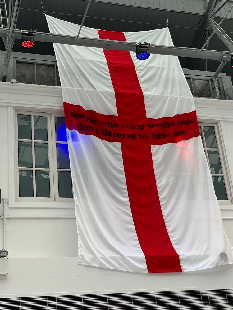 George flag with the legend “Anyone who enjoys waving flags doesn’t deserve one” across the red cross