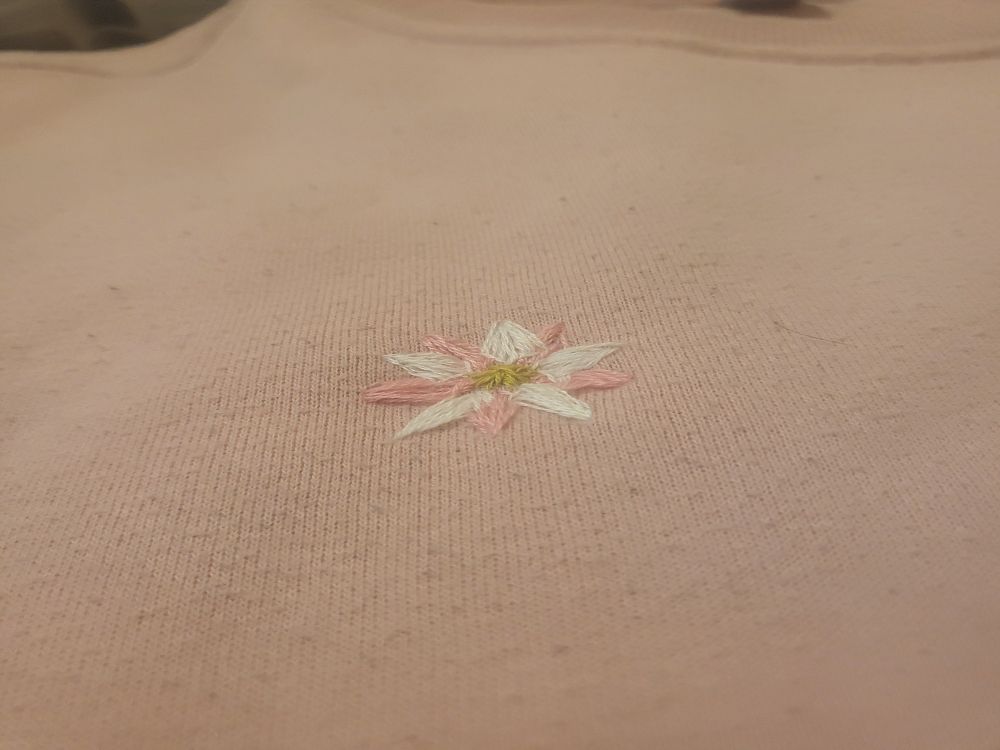 Picture of a pink jumper with a small crude embroidered pink and white flower in the centre of the frame