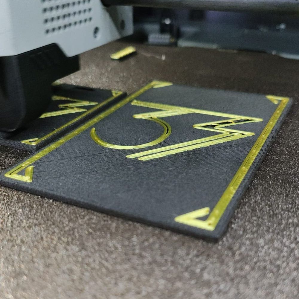 Se ve una pieza impresa en madera negra y filamento dorado con un 33 estilizado