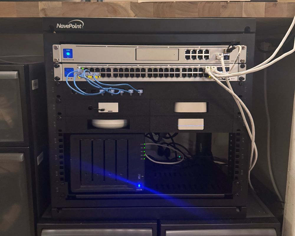 A server rack with a ubiquiti dream machine se and Poe 48 pro switch. Three 3d printed racks for various home hubs and patch connector. On the bottom is a shelf with a Synology DS923+ NAS