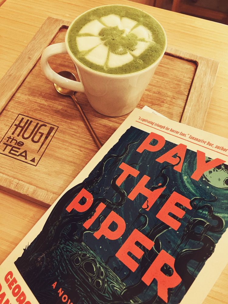 Pay the Piper paperback and a cup of matcha latte on wooden board