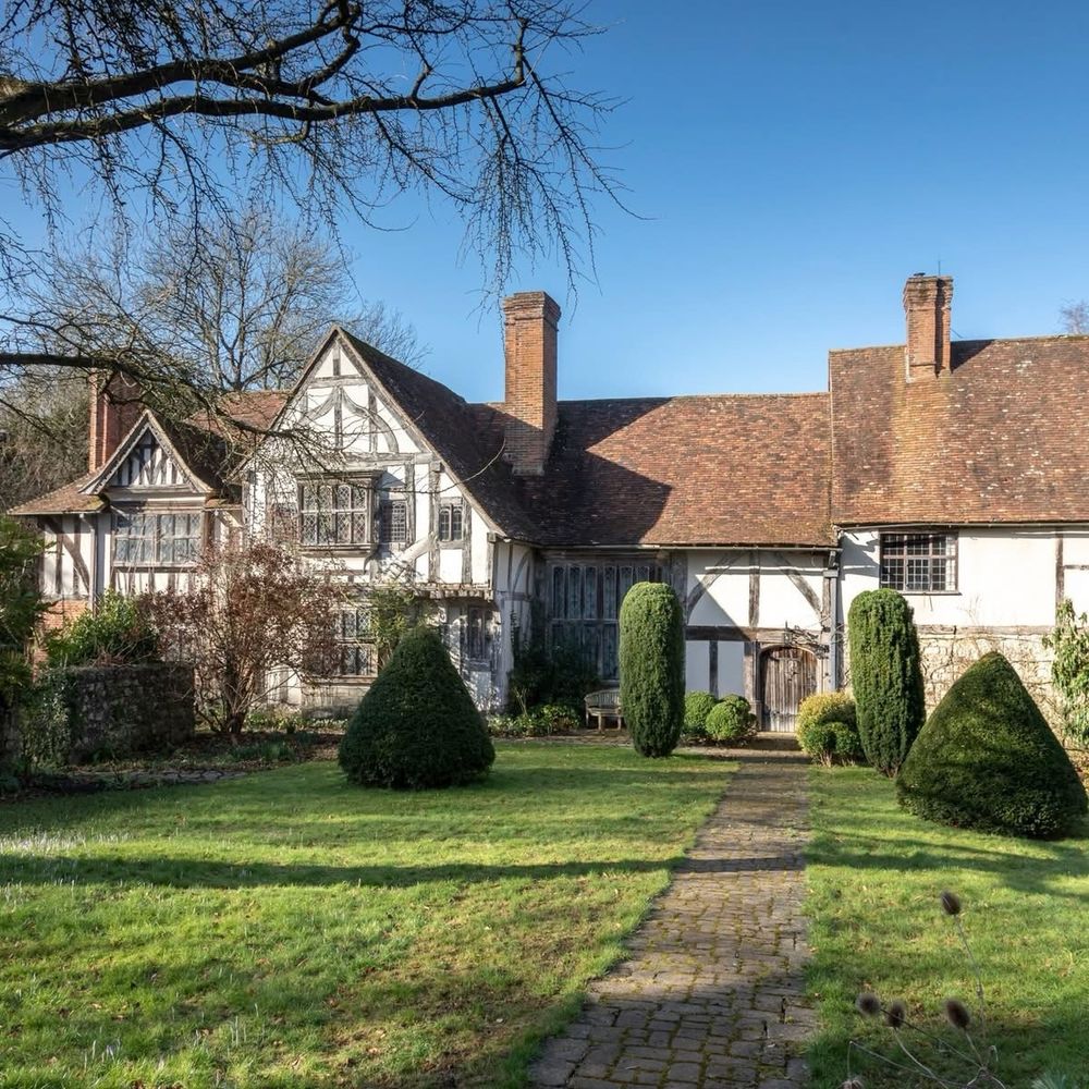 Stoneacre in Kent. A black and white timber framed medieval building with a lawn and shrubs in the foreground. 