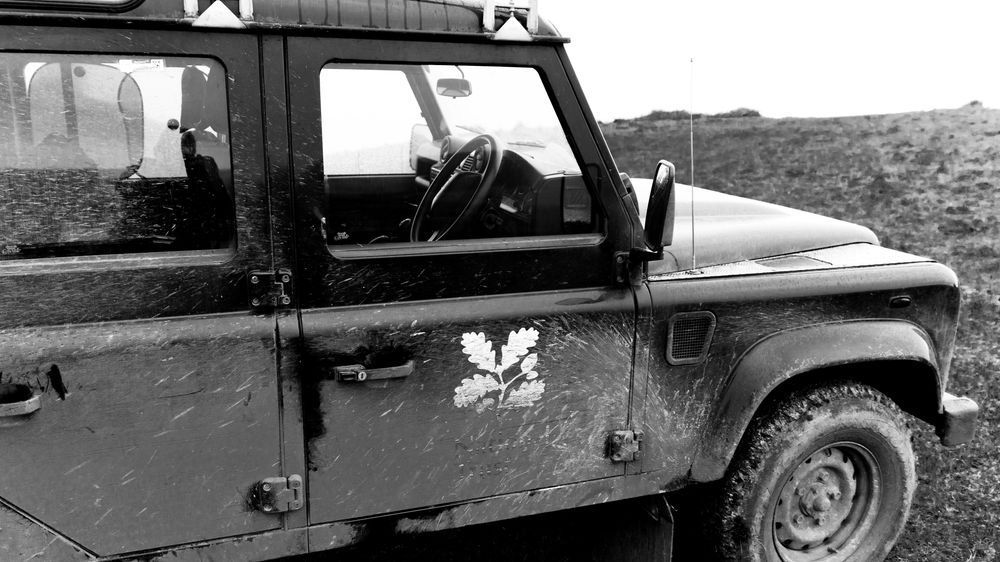 A black and white photo of a landrover with the National Trust oak leaf emblem