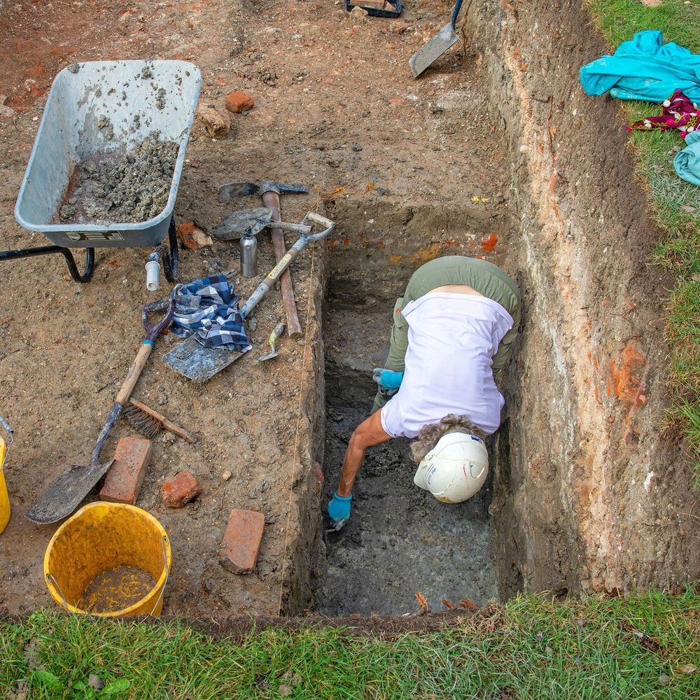 An archaeologist in a trench with a wheelbarrow and buckets and tools ©National Trust/Mike Selby