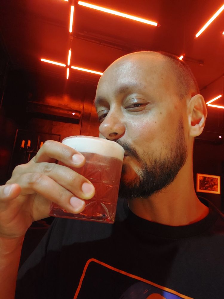 selfie segurando um drink com cachaça e luzes neon vermelho no teto.