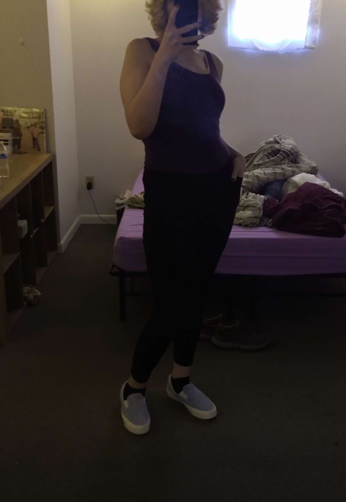 Woman posing in mirror for a selfie to show off new pair of shoes while wearing black leggings and a tank top.