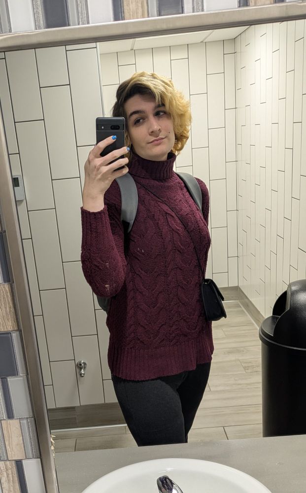 Woman in deep red turtleneck taking selfie in bathroom mirror