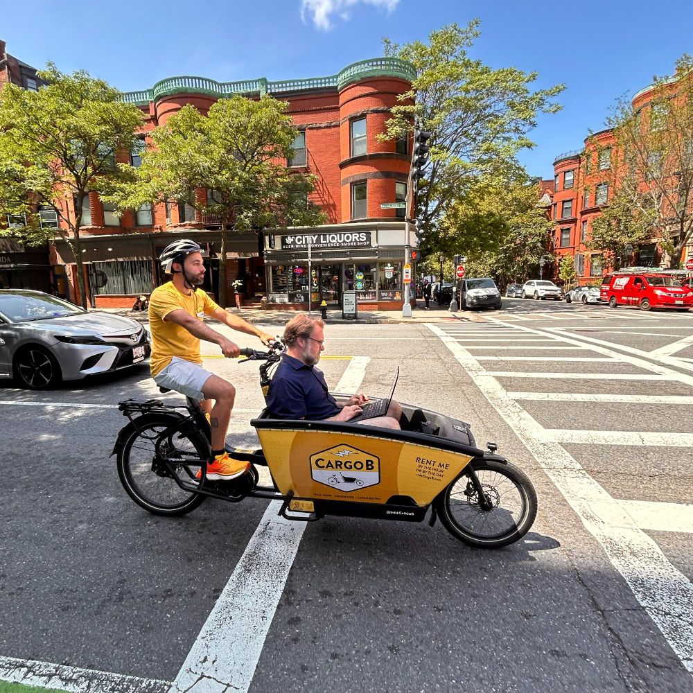 Person working on laptop while riding in the bucket of CargoB electric cargo bike.