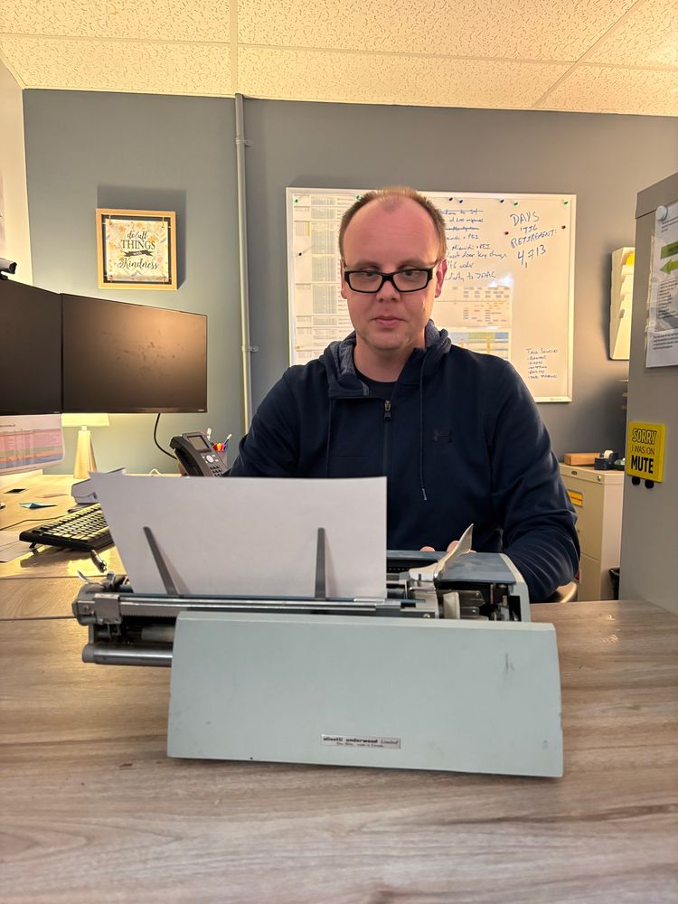 Man sitting at a desk with a typewriter. 