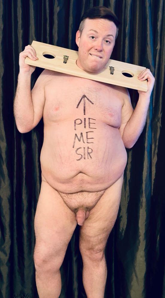 Tyler is completely naked with his neck locked into a pillory. He has “Pie Me Sir” written on his body in permanent marker with an arrow pointing towards his face. 