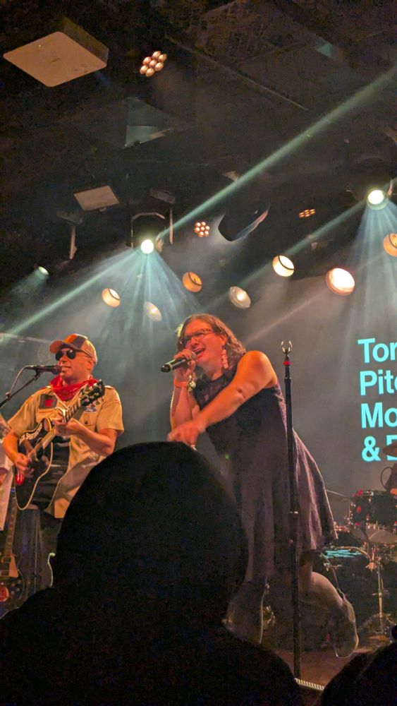 A photo of Tom Morello playing guitar while Evan Greer sings Woody Guthrie's This land is your land.