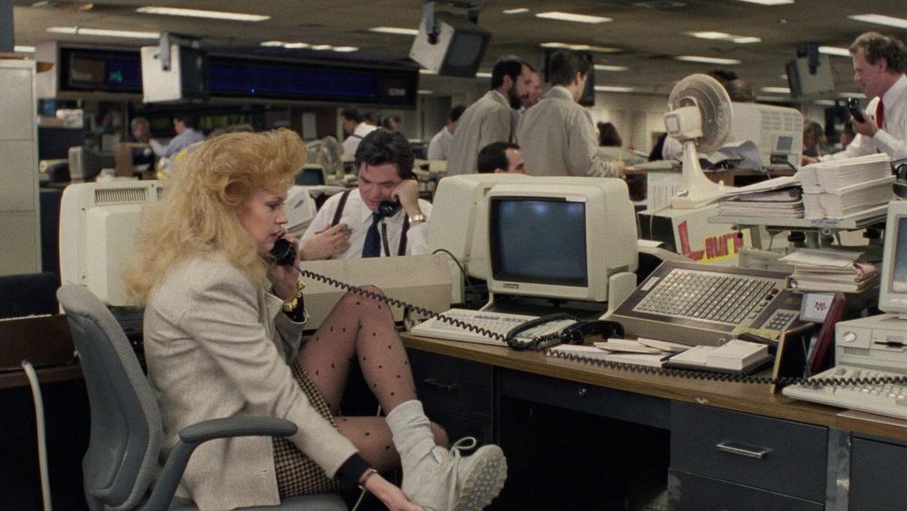 A scene from Working Girl in which Melanie Griffith is changing from sneakers to heels and sitting by an old fashioned computer 