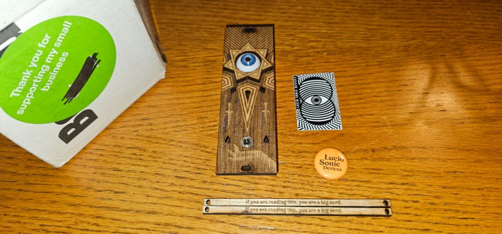 A wooden desk has a wooden eurorack module with a star carved into it with an LED eyeball in the center. There are blank panels that say 