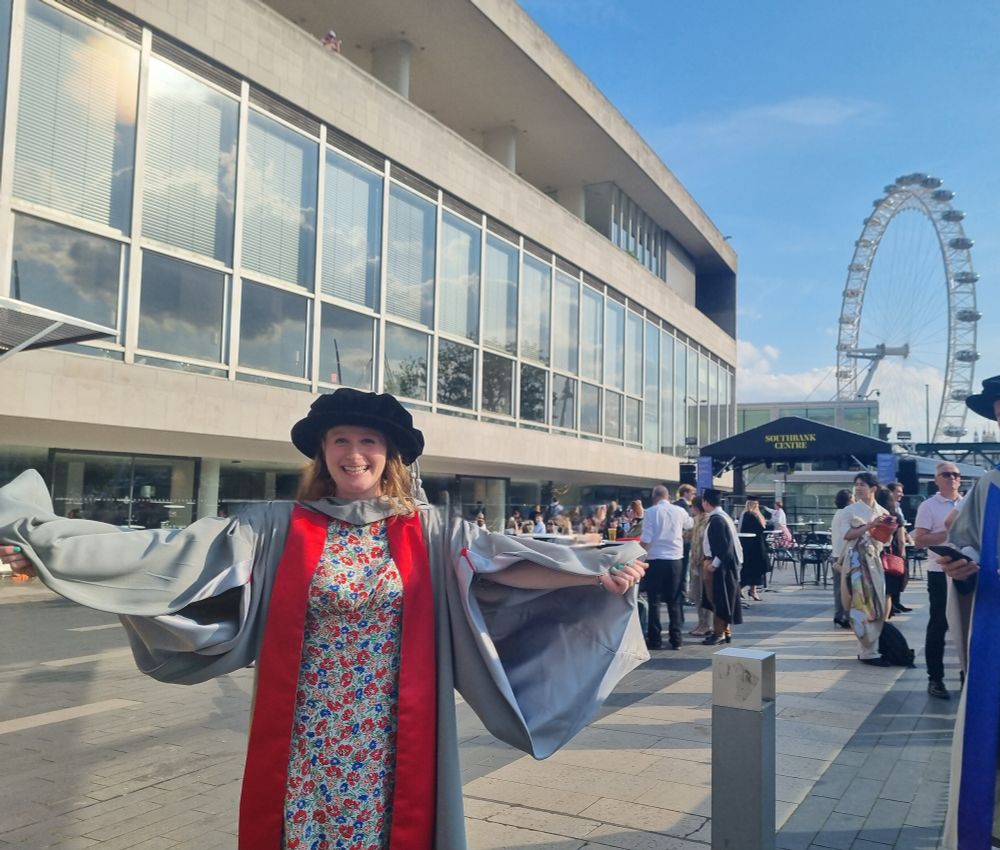 Emily smiling in graduation gown with the London Eye in the background