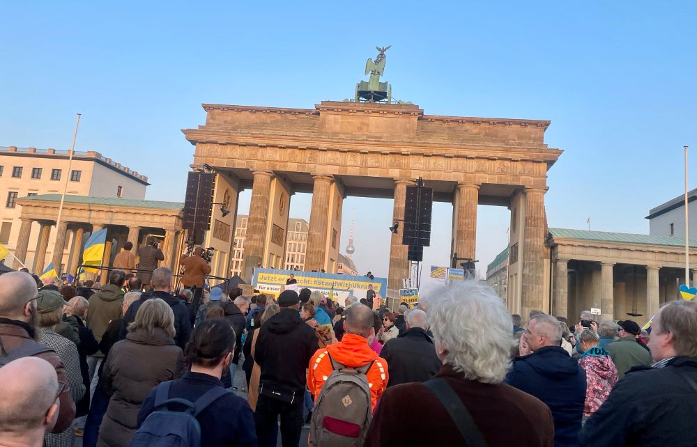 Menschenmenge von dem Brandenburger Tor. Vor den Demonstrierenden eine Redenühne, geschmückt in den blau-gelben Farben der Ukraine. 