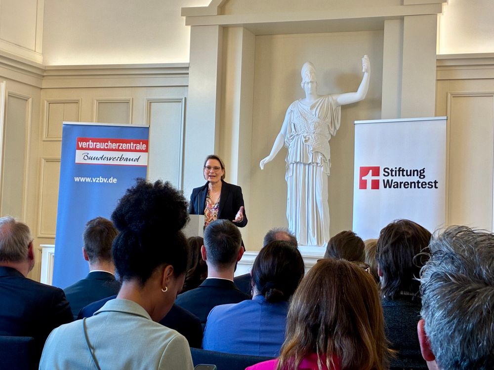 Verbraucherschutzministerin Hubig spricht an einem Pult. Rechts von ihn steht ein Banner der Stiftung Warentest, links eines des Verbraucherzentrale Bundesverbands. 